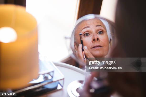 mirror reflection view of mature woman applying make-up on face - eye make up stock pictures, royalty-free photos & images