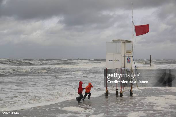 Children run away from the waves during stormy winds on the beach of Wangerooge, Germany, 05 October 2017. Photo: Peter Kuchenbuch-Hanken/dpa