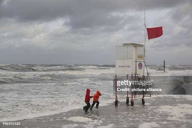 Children run away from the waves during stormy winds on the beach of Wangerooge, Germany, 05 October 2017. Photo: Peter Kuchenbuch-Hanken/dpa