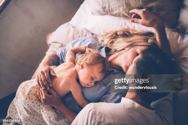 loving couple with sleeping baby kissing in bed - man and woman kissing in bed stock pictures, royalty-free photos & images