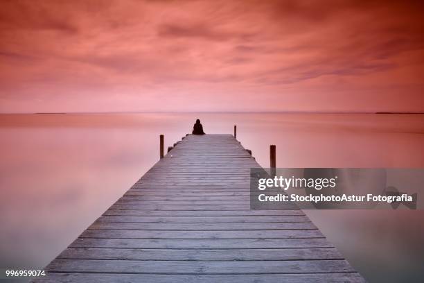 lonely person sitting on pier - fotografia stock-fotos und bilder