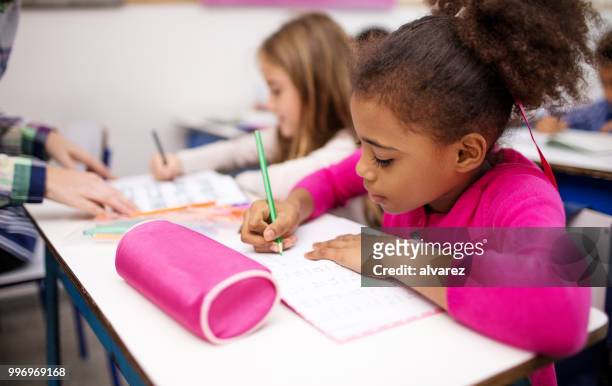 jeune fille écrivant dans livre au pupitre dans la salle de classe - trousse d'écolier photos et images de collection