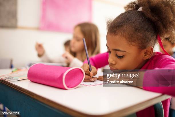 schoolmeisje schrijven in boek bij bureau - etui stockfoto's en -beelden