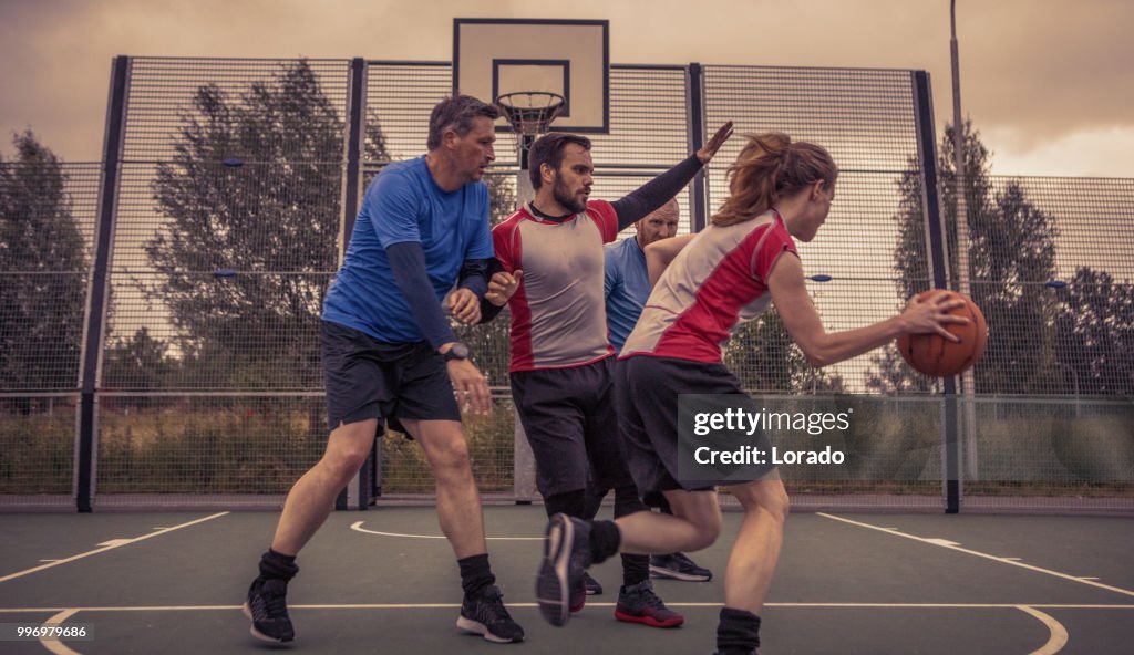 Two adult co-ed basketball teams playing a 2v2 evening pick up game on a street ball court