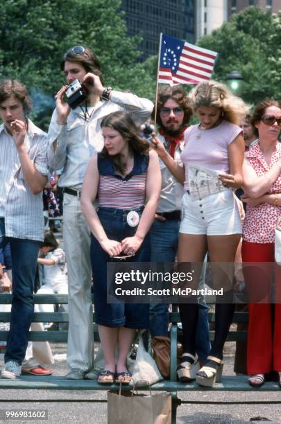 View of people, gathered in downtown Manhattan, as they stand on a park bench during the bicentennial celebrations, New York, New York, July 4, 1976....