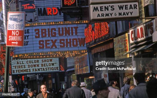 View of cinema marquees that advertise pornographic films, seen over the heads of pedestrians as they walk along 42nd street in Manhattan's Times...