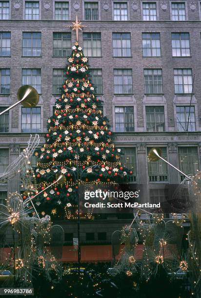 View of a large Christmas tree, as seen through angel statues adorned with Christmas lights on the promenade at Rockefeller Center in midtown...