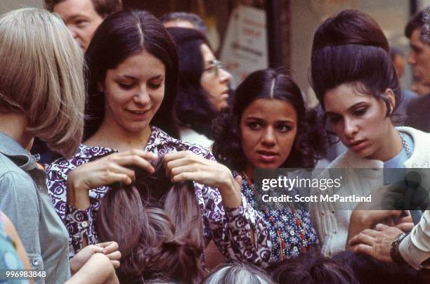 Group of woman examine wigs from sidewalk vendor's display on an unidentified, crowded, Manhattan street, New York, New York, May 1, 1970.