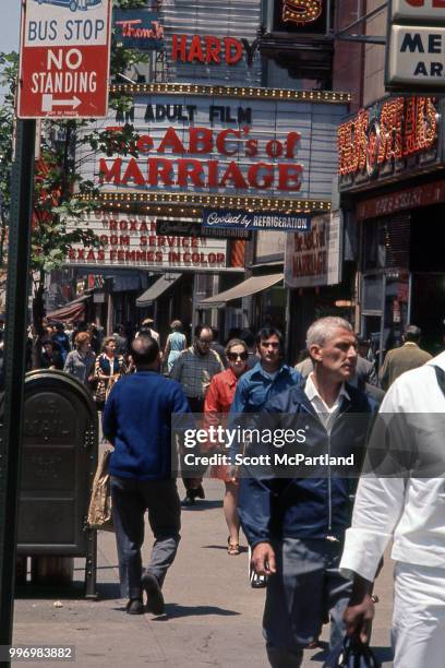 View of pedestrians as they walk along 42nd street, past a row of cinemas that advertise pornographic films in Manhattan's Times Square, New York,...