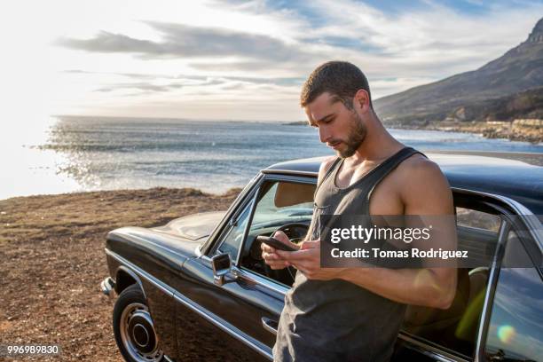 young man with car using cell phone at the coast at sunset - young adult mobile phone serious stock pictures, royalty-free photos & images