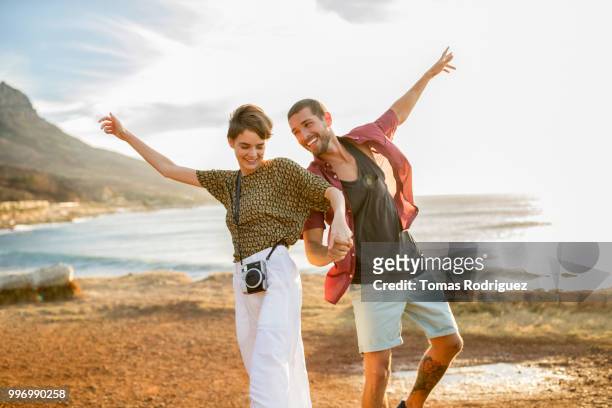 happy cheerful couple hand in hand at the coast at sunset - frauen mit fotoapparat stock-fotos und bilder