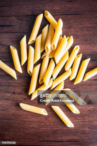 heap of uncooked whole wheat penne italian pasta, top view. pasta pattern. food background. - whole wheat penne pasta stock pictures, royalty-free photos & images
