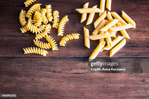 variety of types and shapes of dry italian pasta - fusilli and penne, top view. uncooked whole wheat italian pasta. image with copy space. - whole wheat penne pasta stock pictures, royalty-free photos & images