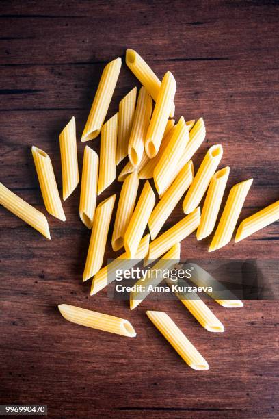 heap of uncooked whole wheat penne italian pasta, top view. pasta pattern. food background. - whole wheat penne pasta stock pictures, royalty-free photos & images