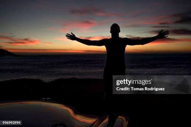 silhouette of a man standing at the coast at dusk with outstretched arms - auto silhouette stock-fotos und bilder