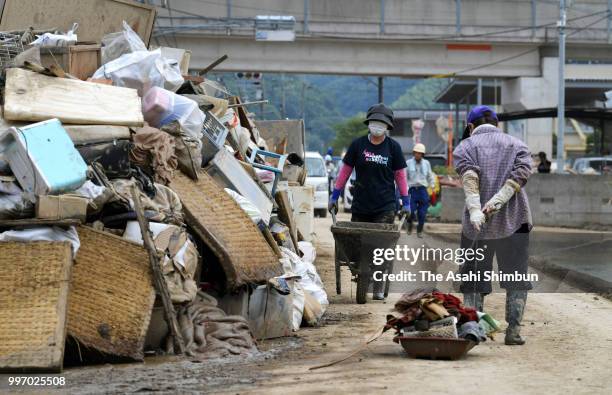 People wearing masks take debris at a collecting point after submerged by flood on July 12, 2018 in Kurashiki, Okayama, Japan. The death toll from...