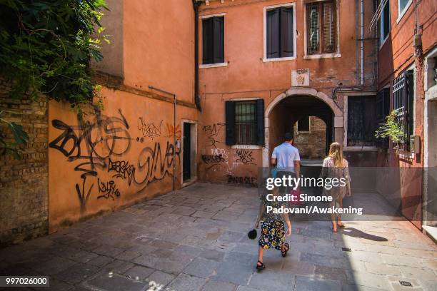 Tourists walk in a calle to reach St. Mark square from railway station, where there are graffiti and tags on the walls, through San Polo district, on...