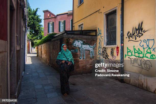 Woman walks in Calle Contarina, where there are graffiti and tags on the walls, on the way that connect University Ca' Foscari of Venice to railway...