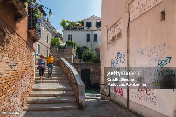 Tourists cross the bridge of Avogaria, to walk in Calle de l'Avogaria, where there are graffiti and tags on the walls, on the way to reach San...