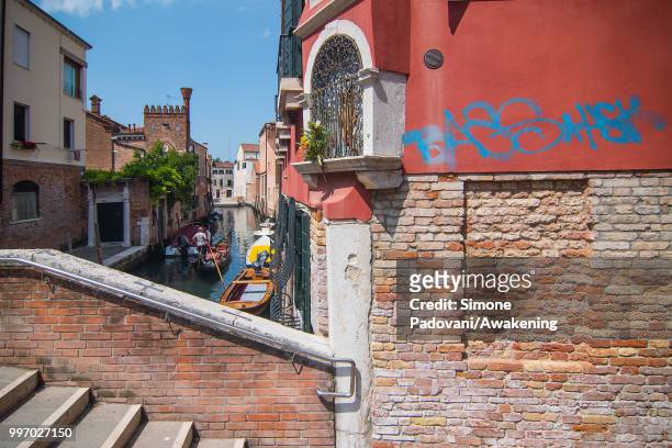 Gondola sails the canal of Avogaria, where there is a tag on the wall close to a votive shrine, through Dorsoduro district, on July 12, 2018 in...
