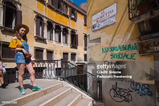 Girl crosses the Del Megio bridge, where there are graffiti and tags on the walls, through Santa Croce district, on July 12, 2018 in Venice, Italy....