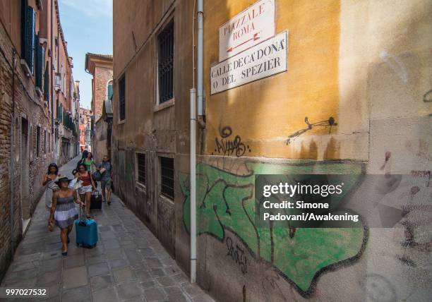 Tourists walk in Calle De Ca' Donà, where there are graffiti and tags on the walls, on the way that connects the bus station, Piazzale Roma, to...