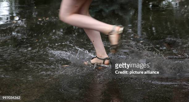 July 2018, Germany, Neuenhagen: A young woman swiftly crosses a flooded street during temperatures of about 16 degrees. According to meteorologists...