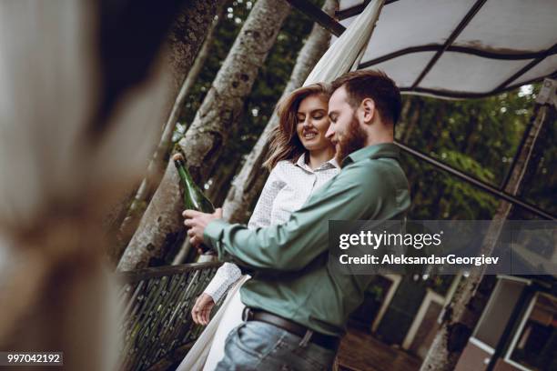 young couple opening champagne bottle for anniversary - drunk husband stock pictures, royalty-free photos & images