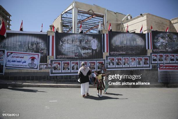 Yemeni man and a girl look at pictures of victims, hung on the walls surrounding the destroyed funeral hall, during a protest to mark the 1st...