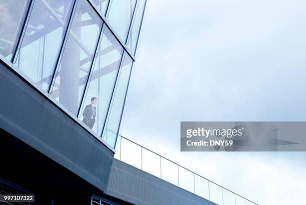 businessman stands inside building and looks out through window - skyscraper window stock pictures, royalty-free photos & images