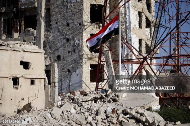 The Syrian national flag rises in the midst of damaged buildings in Daraa-al-Balad, an opposition-held part of the southern city of Daraa, on July...