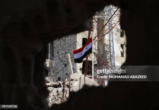 The Syrian national flag rises in the midst of damaged buildings in Daraa-al-Balad, an opposition-held part of the southern city of Daraa, on July...