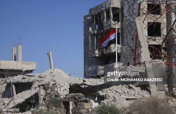 The Syrian national flag rises in the midst of damaged buildings in Daraa-al-Balad, an opposition-held part of the southern city of Daraa, on July...