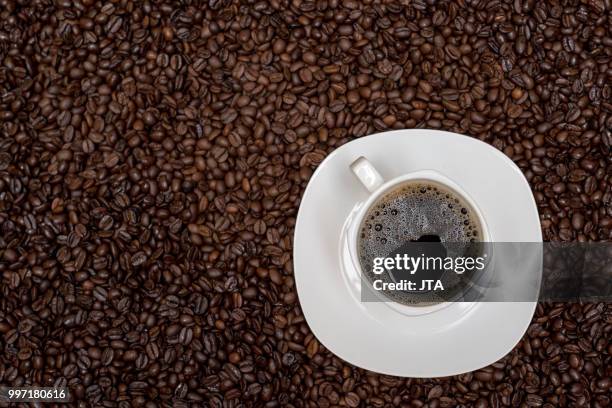 coffee beans background and white cup with hot drink - coffee drink stock pictures, royalty-free photos & images