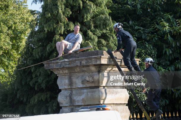Police bring a man down from a plinth as protesters gather at the gates of Blenheim Palace where US President Donald Trump is due at a evening...