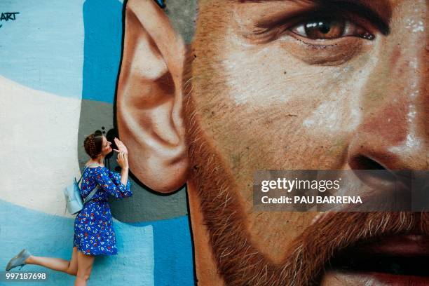 Woman poses next to a graffiti by Cobre Art depicting Barcelona's Argentinian forward Lionel Messi in Barcelona, on July 12, 2018. / RESTRICTED TO...