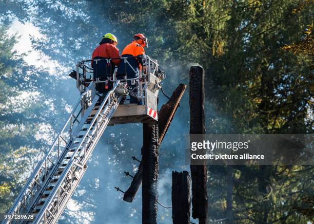 Two firefighters standing on an aerial ladder in front of the smoking remains of the Goether Tower and sawing them off in Frankfurt am Main, Germany,...