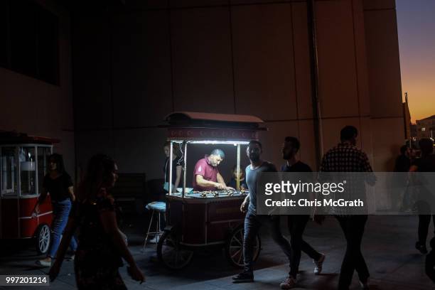 People walk past a man selling roasted chestnuts from a cart in Taksim Square on July 12, 2018 in Istanbul Turkey. Following Turkey's President Recep...