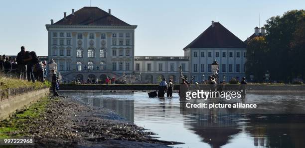 Fisherman standing during the traditional fishing out in the Nymphenburger canal with a castle to be seen in the background in Munich, Germany, 14...