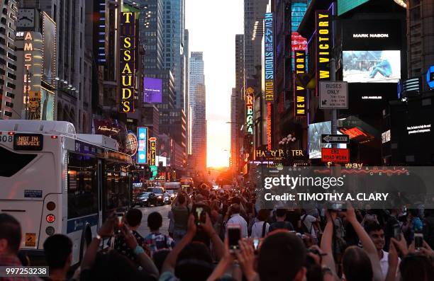 People take photos with their mobile phones as the sun sets as seen from 42nd street in Times Square in New York City on July 12, 2018 during...