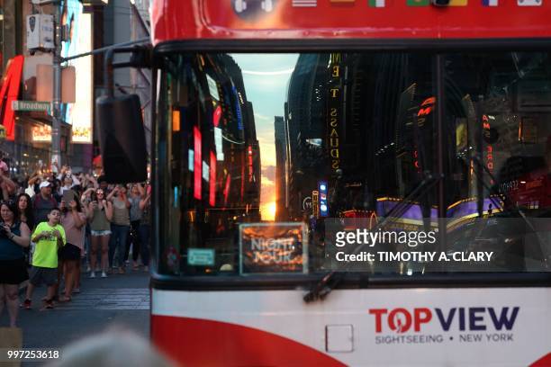 People take photos with their mobile phones as the sun sets as seen from 42nd street in Times Square in New York City on July 12, 2018 during...