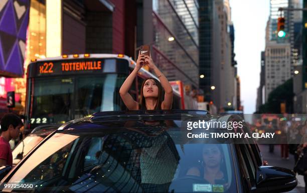 Woman takes a photo from the sunroof of a car as the sun sets as seen from 42nd street in Times Square in New York City on July 12, 2018 during...