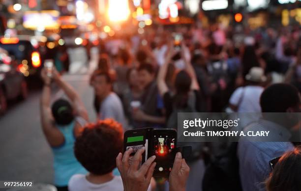 People take photos with their mobile phones as the sun sets as seen from 42nd street in Times Square in New York City on July 12, 2018 during...