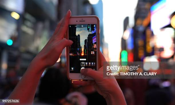Woman takes a photo with her mobile phone as the sun sets as seen from 42nd street in Times Square in New York City on July 12, 2018 during...
