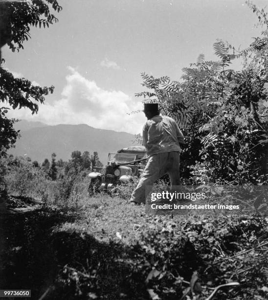 Orient Expedition of the Austrian Mr. Von Kummer: A man is standing near to a lane and is cutting the shrubs. In the background is a car of the...