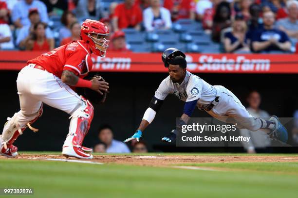 Dee Gordon slides safely at home scoring on an RBI single hit by Kyle Seager of the Seattle Mariners as Martin Maldonado of the Los Angeles Angels of...