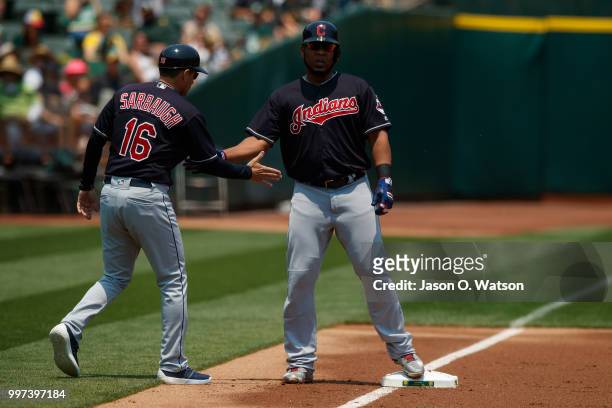 Edwin Encarnacion of the Cleveland Indians is congratulated by third base coach Mike Sarbaugh during the first inning against the Oakland Athletics...