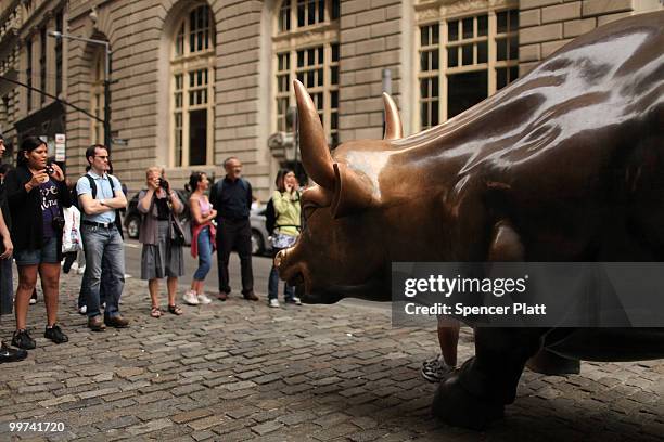 People pose for pictures beside the Wall Street bull, a bronze bull statue that symbolizes a "bull market" on May 17, 2010 in New York, New York....