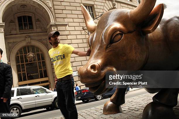 People pose for pictures beside the Wall Street bull, a bronze bull statue that symbolizes a "bull market" on May 17, 2010 in New York, New York....
