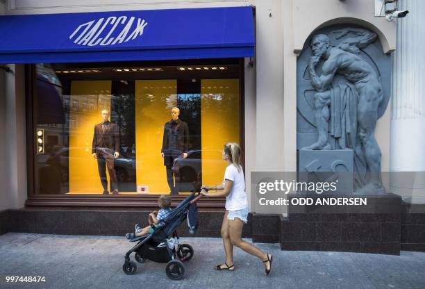 Woman pushes a stroller as she walks past the statue of a worker bearing a hammer and sickle on a Soviet-era building converted into a shopping mall...